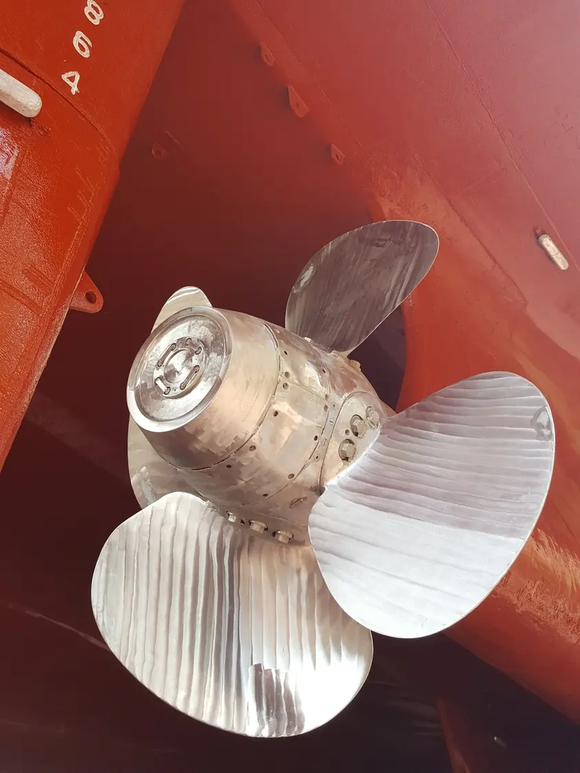 Propeller and rudder of a ship in dry dock, the underwater hull repainted and the anodes visible on the shell plating