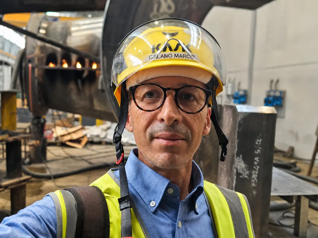 Capt. Marco Galano, Technical Director of DO.G.MA. Service, photographed on site in helmet and high-visibility vest in a steel fabrication area