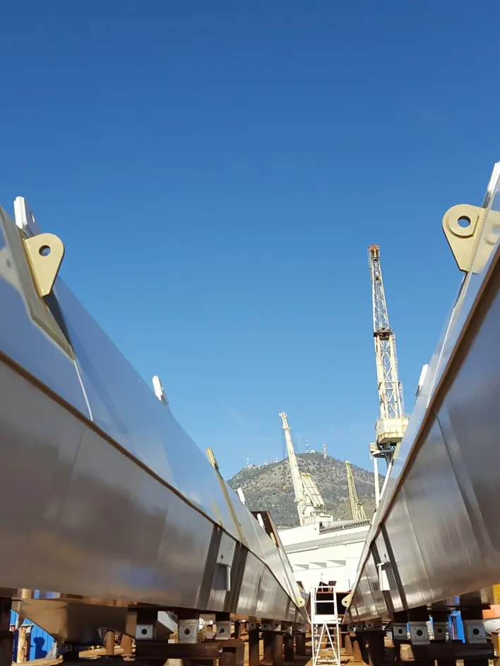 Coated structural steel beams lined up on trestles on site, with cranes in the background