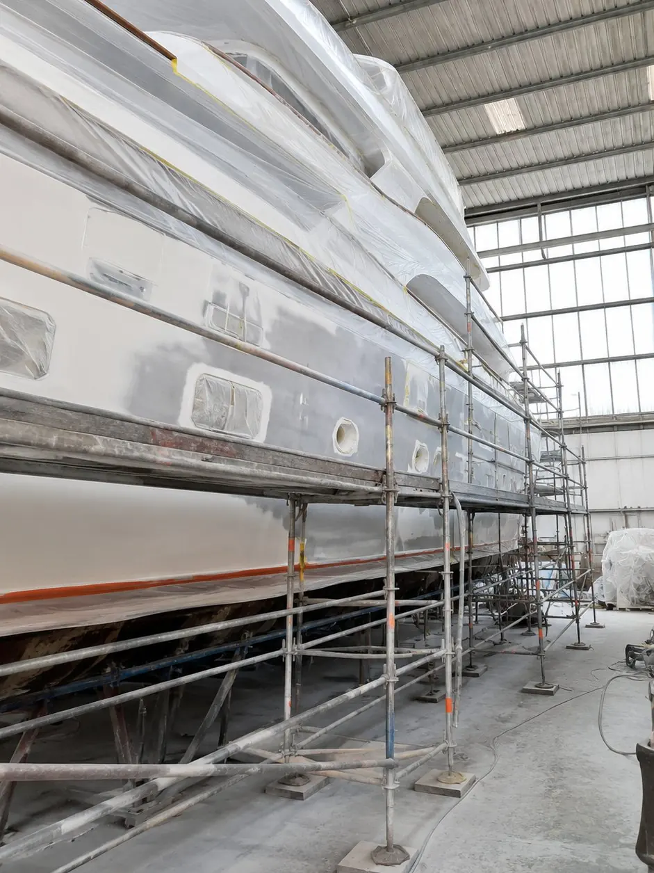 Yacht in refit all'interno di un capannone: fiancata mascherata con teli protettivi e ponteggi montati lungo tutta la lunghezza