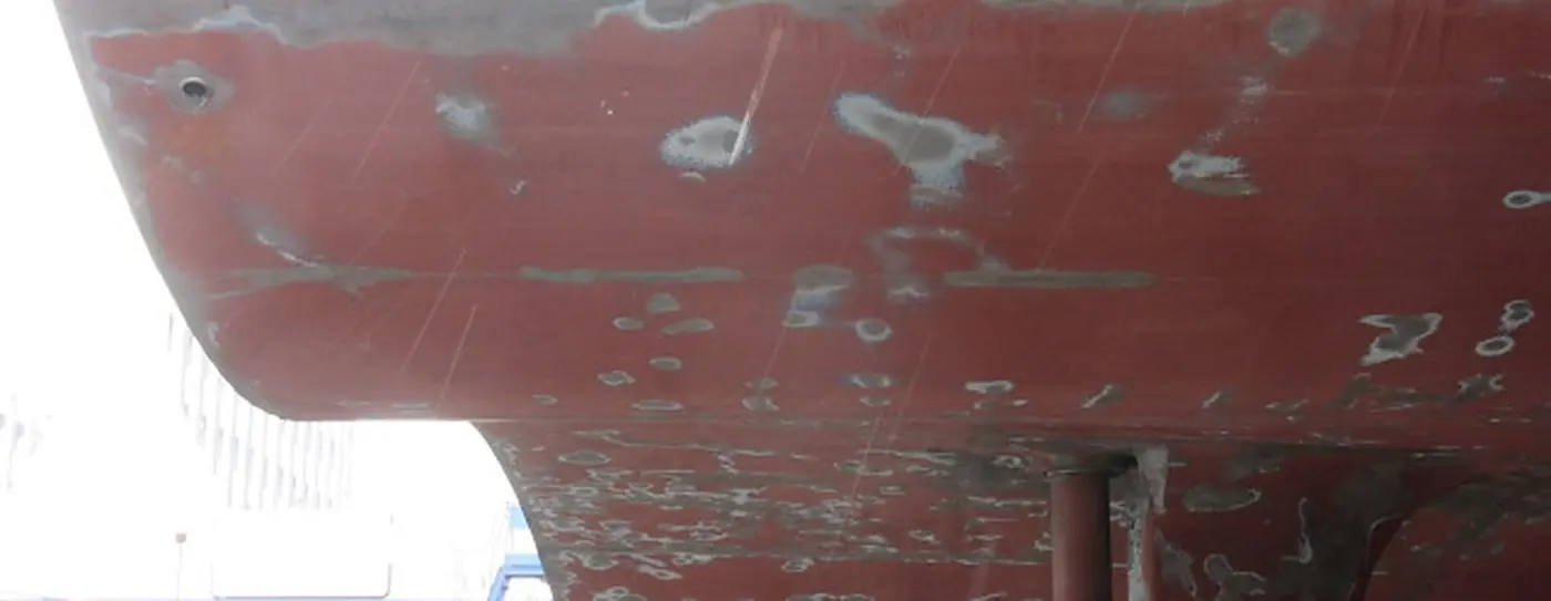 Opera viva di una nave in bacino con il rivestimento distaccato a chiazze e l'acciaio in vista, prima del ripristino