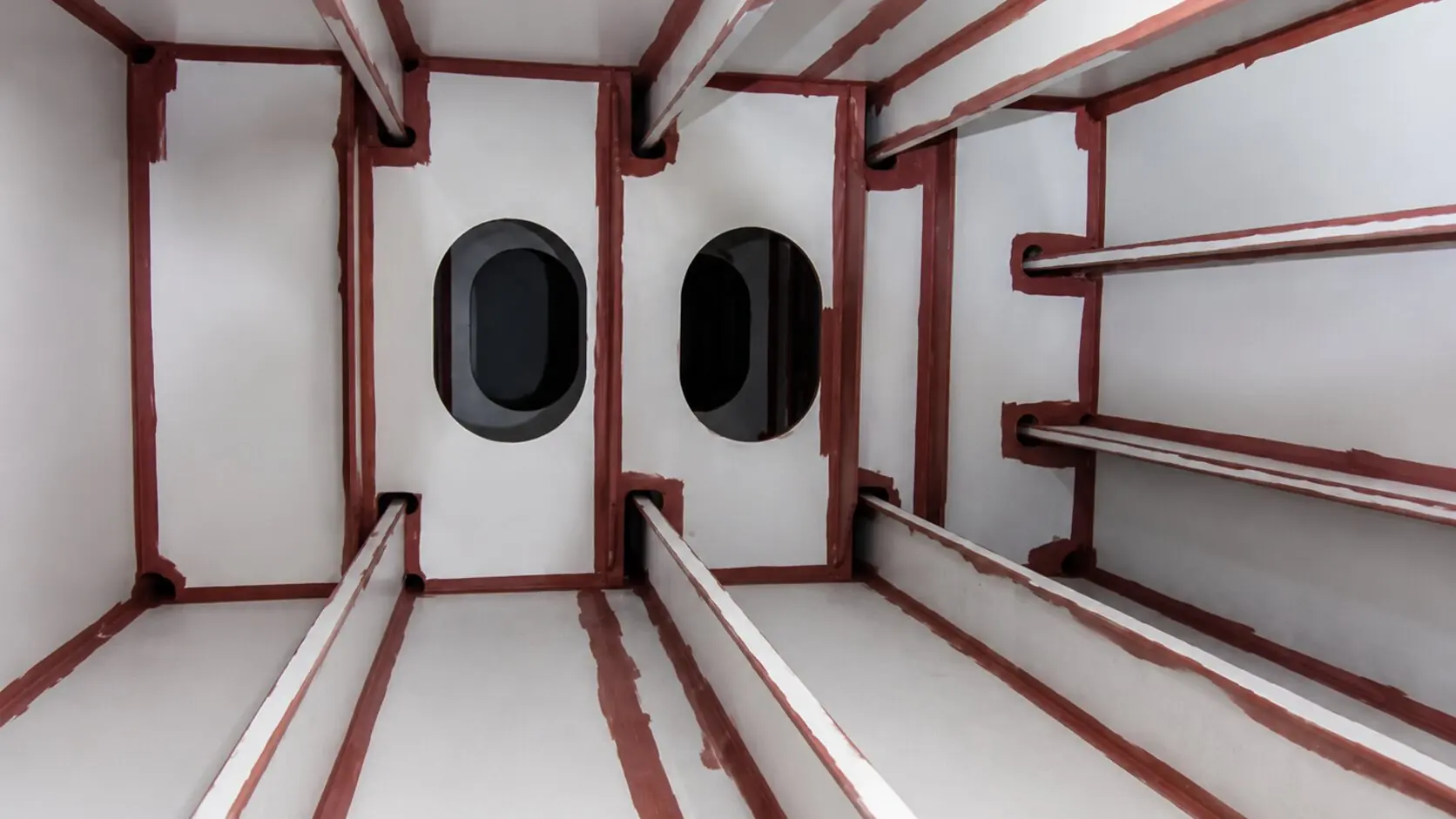 Interior of a white-coated tank with the red stripe coat brush-applied to stiffeners, corners and edges, and two manholes in the bulkhead