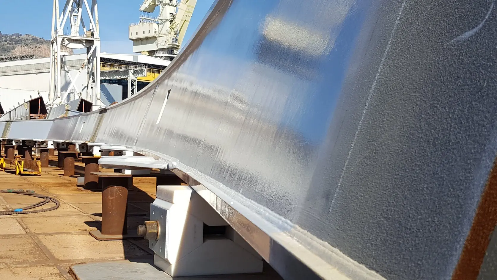 Structural steel beam after thermal spray metallising, the matt grey surface seen in raking light with the yard behind